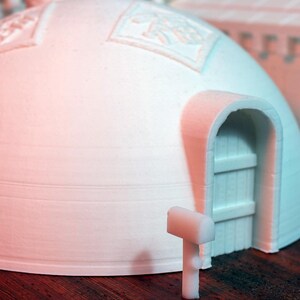 May include: A white, dome-shaped structure with a door and a small white mailbox in front. The structure has a textured surface and appears to be made of plastic.