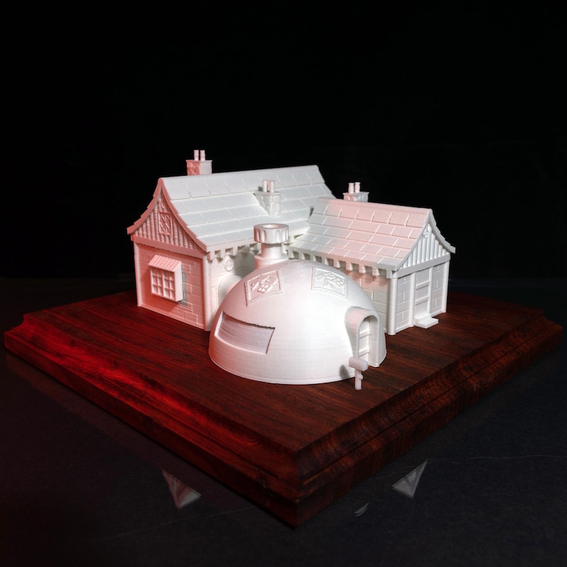 May include: A white 3D printed model of a house with a domed roof and a smaller attached building. The model is sitting on a dark wood base.