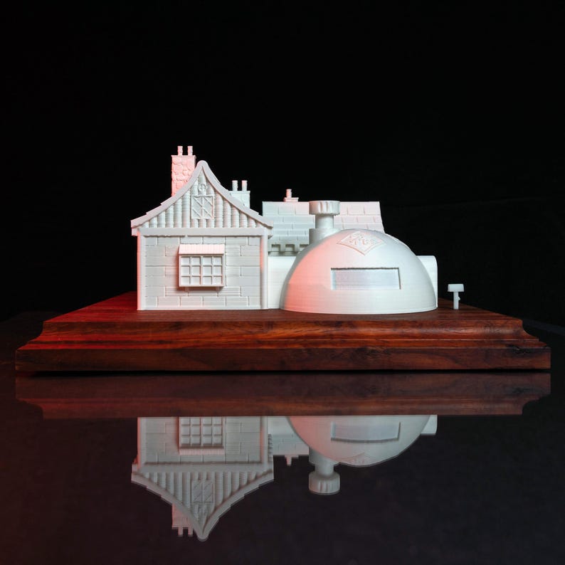 May include: A white 3D printed model of a building with a dome roof and a smaller building attached to the side. The model is sitting on a wooden base.