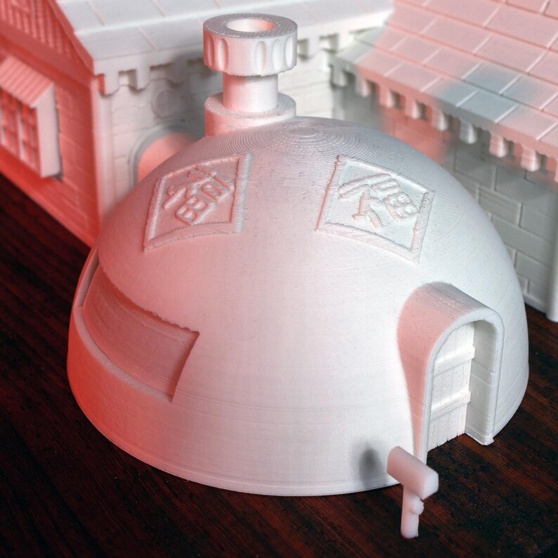 May include: White 3D printed model of a dome-shaped house with a small door and a chimney. The dome has two square symbols on it, one with the Chinese character for "happiness" and the other with the Chinese character for "fortune".