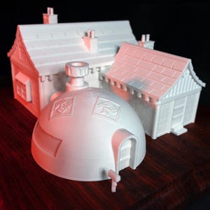 May include: White 3D printed model of a small house with a domed roof and a chimney. The house has a white brick exterior and a white tiled roof. The house is sitting on a wooden base.