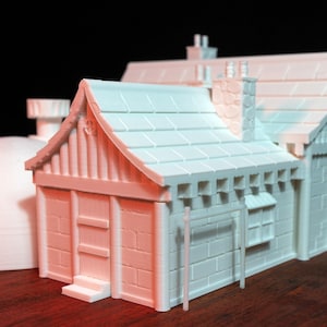 May include: A white 3D printed model of a small building with a gabled roof, a chimney, and a door. The building has a brick facade and a wooden frame.