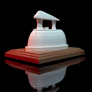 Puede incluir: Un modelo blanco de hierro antiguo impreso en 3D sobre una base de madera. El hierro está sobre una superficie oscura.