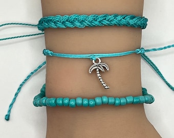 May include: Three turquoise bracelets with a palm tree charm. The top bracelet is braided, the middle bracelet is a simple string, and the bottom bracelet is made of small beads.