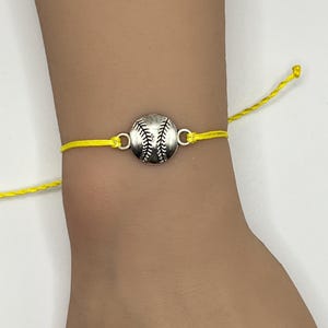 May include: A yellow string bracelet with a silver baseball charm.