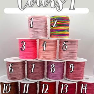 Puede incluir: Carretes de cord&oacute;n colorido en varios tonos, incluyendo rosa, rojo y marr&oacute;n. La imagen est&aacute; etiquetada como "Colors 1" y presenta carretes numerados, ideales para manualidades o bisuter&iacute;a. El cord&oacute;n est&aacute; bien enrollado en carretes blancos.