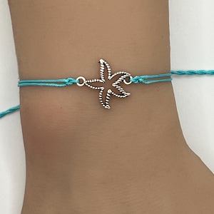 May include: A turquoise blue string bracelet with a silver starfish charm.
