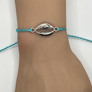 May include: A turquoise blue string bracelet with a silver seashell charm.