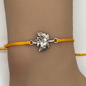 May include: A yellow string bracelet with a silver leaf charm.