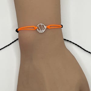 May include: A black and orange string bracelet with a silver basketball charm.