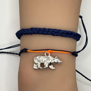 May include: A blue and orange friendship bracelet with a silver bear charm.