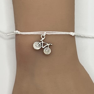 May include: White string bracelet with a silver bicycle charm.