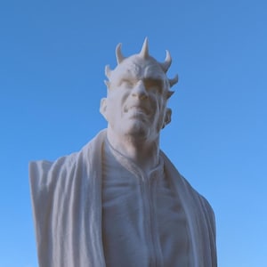 Puede incluir: Busto blanco impreso en 3D de un personaje con cuernos y una expresión severa. El busto lleva una túnica y está montado sobre una base redonda.