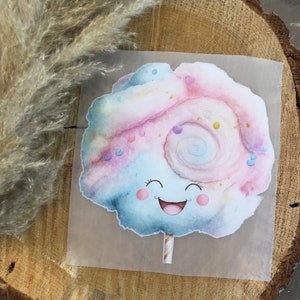 Könnte beinhalten: Eine bunte Illustration von Zuckerwatte mit einem lächelnden Gesicht und Streuseln. Die Zuckerwatte ist auf einem Stiel und hat ein Spiraldesign.
