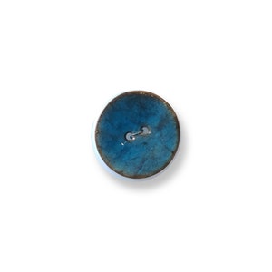 Könnte beinhalten: Ein blauer Keramik-Knopf mit braunem Rand. Der Knopf hat zwei Löcher in der Mitte.