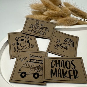 Könnte beinhalten: Fünf braune Karten mit schwarzem Text und Illustrationen. Die Karten sagen "Ich bin EINZIGARTIG und SCHON", "Tatii Tataaa!" mit einem gezeichneten Feuerwehrauto, "Ich werde geliebt" mit einem Regenbogen und "CHAOS MAKER". Die fünfte Karte zeigt einen gezeichneten Bären mit Sternen.