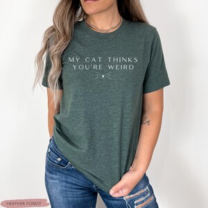 May include: A green t-shirt with the text "My cat thinks you're weird" in white lettering. A small cat whisker design is below the text.