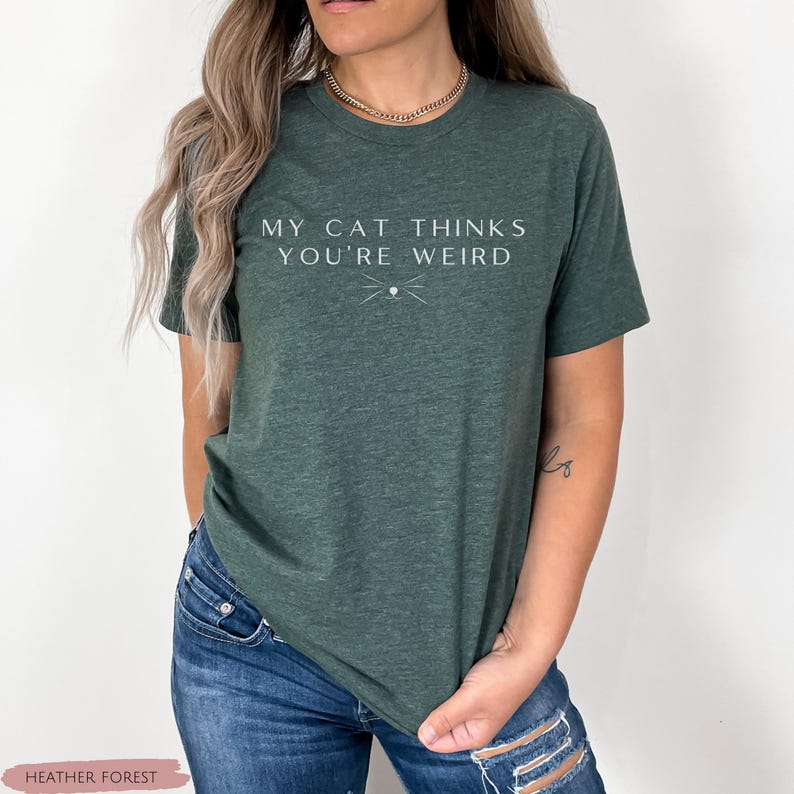 May include: A green t-shirt with the text "My cat thinks you're weird" in white lettering. A small cat whisker design is below the text.