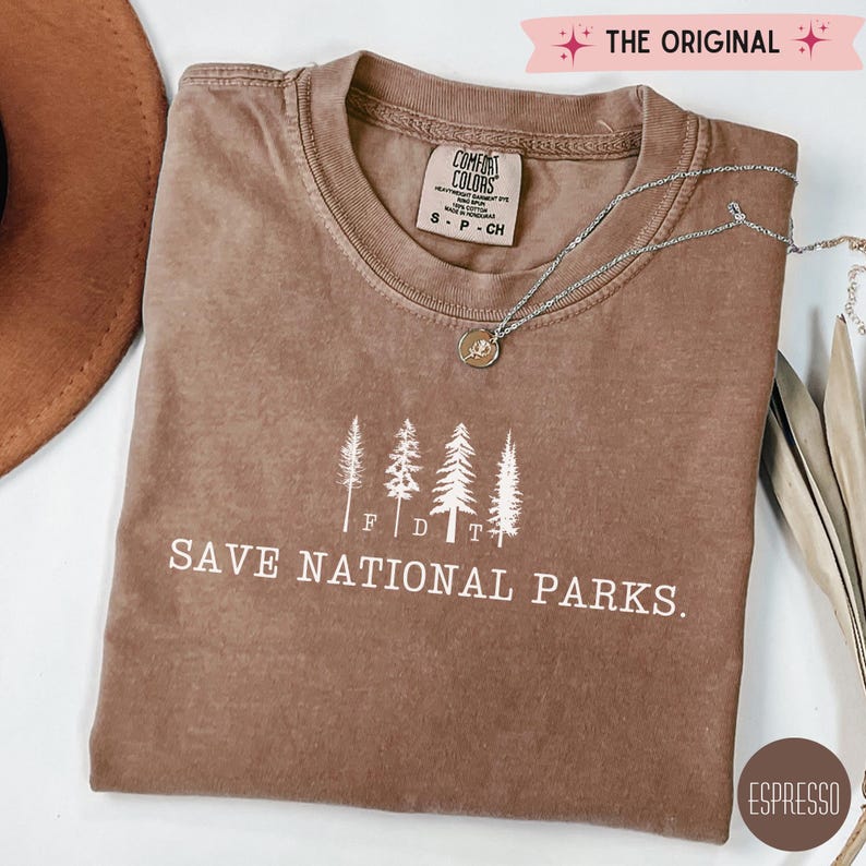May include: A brown t-shirt with a white graphic of trees and the text "Save National Parks." The shirt has a distressed look and is made of a soft, comfortable fabric.