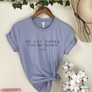 May include: A heather blue t-shirt with the text "My cat thinks you're weird" and a small cat face graphic.