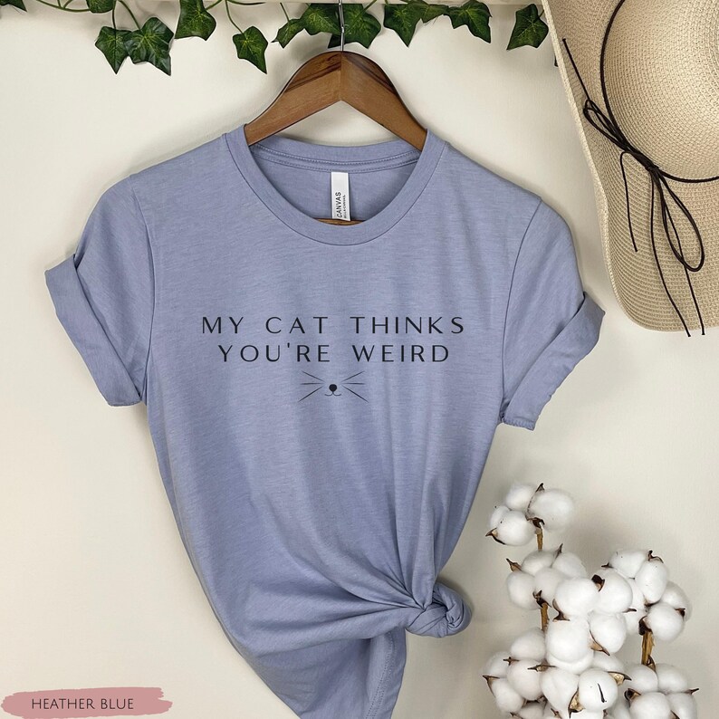 May include: A heather blue t-shirt with the text "My cat thinks you're weird" and a small cat face graphic.