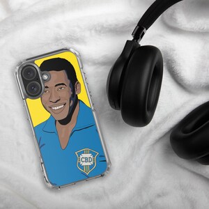 May include: Clear phone case featuring a vibrant illustration of a smiling person in a blue shirt against a yellow backdrop. The case has a logo with the letters "CBD". Black headphones are visible in the background.
