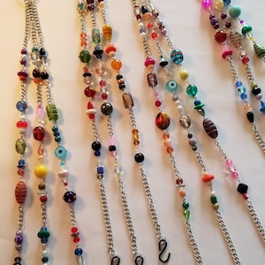 May include: A collection of beaded eyeglass chains. Each chain features a silver-colored chain with a variety of colorful beads in different shapes and sizes. The chains have a loop at the top and black rubber loops at the bottom for attaching to glasses.