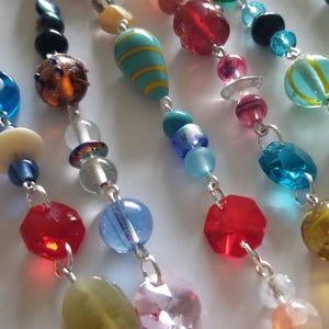 May include: Close-up of colorful beaded strands. The beads are various shapes and sizes, including round, faceted, and oblong. Colors include red, blue, green, yellow, and pink. The beads are strung on silver-colored wire.