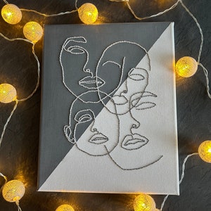 Peut inclure: Une toile noire et blanche avec un dessin au trait de trois visages. Les visages sont dessinés dans un style minimaliste et se chevauchent. La toile est divisée en diagonale, la moitié supérieure étant noire et la moitié inférieure étant blanche.