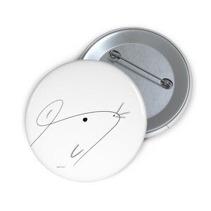 May include: White button pin with a minimalist black line drawing of a mouse. The mouse's head is depicted with a single continuous line, featuring an ear, eye, and whiskers. The pin is round and has a metal backing.