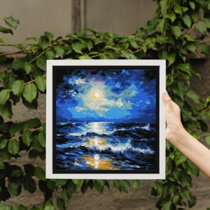 May include: Square framed painting of a moonlit ocean scene. The artwork features a bright yellow moon, dark blue clouds, and white-capped waves. A small lighthouse is visible in the distance. The frame is white.