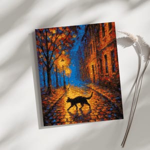 May include: A framed art print depicting a nighttime street scene. A black cat walks along a cobblestone path illuminated by streetlights. The buildings and trees are rendered in warm tones of orange and brown against a dark blue sky.