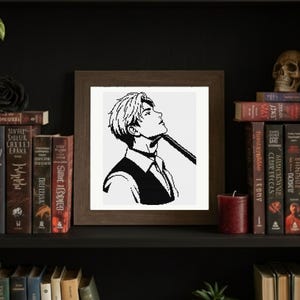 May include: A framed black and white illustration of a person looking upwards, wearing a vest and tie. The artwork is displayed on a dark wooden shelf with books, a candle, and a skull.