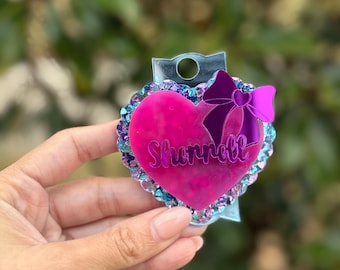 May include: A pink heart-shaped acrylic keychain with a purple bow and glitter accents. The name "Shonnell" is written in white lettering on the heart.