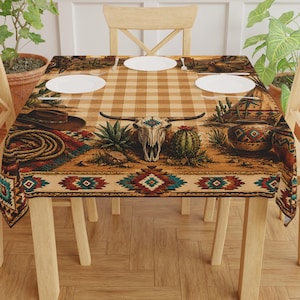 May include: A rectangular tablecloth with a Western theme, featuring a tan and brown checkered pattern. The design includes a bull skull, cacti, a cowboy hat, and a rope. The border has a Southwestern geometric pattern. Four white plates are on the table.