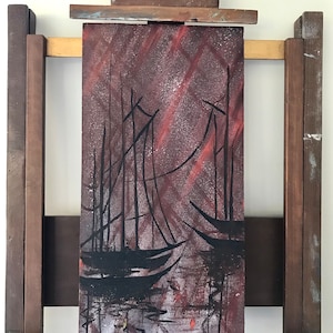 May include: A painting on an easel depicting a dark silhouette of three sailboats on a red and gray background.