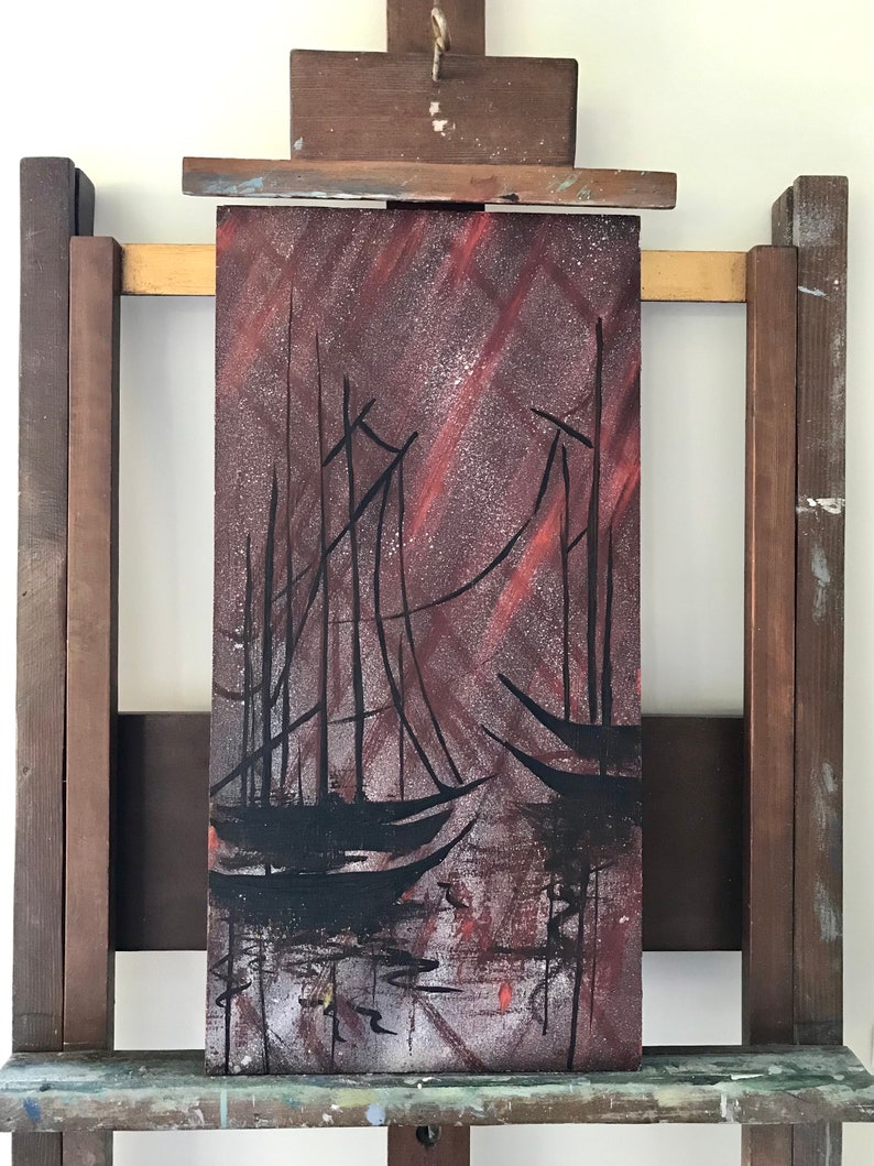 May include: A painting on an easel depicting a dark silhouette of three sailboats on a red and gray background.