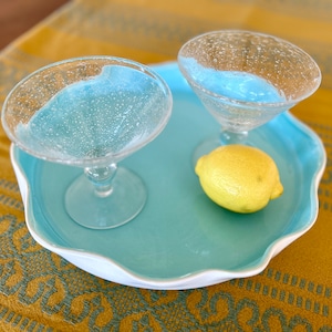 Puede incluir: Una bandeja de cerámica azul y blanca con dos copas de martini de vidrio transparente y un limón amarillo en la parte superior.