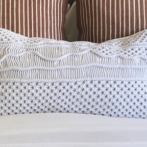 May include: White crocheted pillow with a geometric pattern. The pillow is rectangular and has a soft, textured surface.