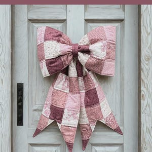 May include: A large, quilted bow in shades of pink and burgundy hangs on a white door. The bow is made of patchwork squares and has long, pointed tails. Text at the top reads "THE BIG GIANT QUILTED BOW".
