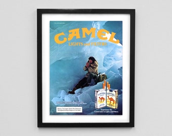 May include: Framed vintage Camel Lights and Filters advertisement. The ad features a person in a cold environment, with the brand name in yellow and a pack of cigarettes. The text reads "Experience the Camel taste in Lights and Filters."