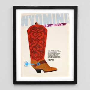 May include: Framed vintage poster featuring a stylized illustration of a cowboy boot. The boot is primarily red with ornate detailing, a brown strap, and a blue spur. Text at the top reads "WYOMING IS 307 COUNTRY."