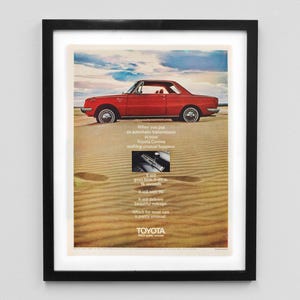 May include: A vintage advertisement for a red Toyota Corona car driving on a sandy beach. The text reads "When you put an automatic transmission in your Toyota Corona nothing unusual happens." It also says "It has great gas mileage, it's smooth, it delivers 90% of its mileage." and "Which for most can be pretty unusual."