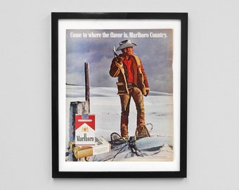 May include: Framed vintage Marlboro cigarette advertisement. The image shows a cowboy in a snowy scene with the text "Come to where the flavour is. Marlboro Country." Packs of cigarettes are in the foreground.