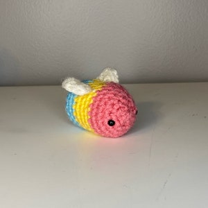 May include: A crocheted bee toy with blue, yellow, and pink stripes. The bee has black eyes and white wings.