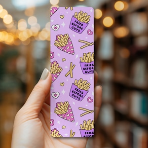 May include: Purple bookmark with a repeating pattern of french fries in pink containers with the text "Fries Before Guys" on a white background.  The background also has pink hearts and white stars.