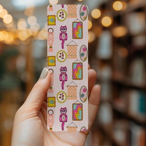 May include: A pink bookmark with a repeating pattern of a pink cat clock, a rainbow-colored picture frame, a macrame wall hanging, and a small floral picture frame.