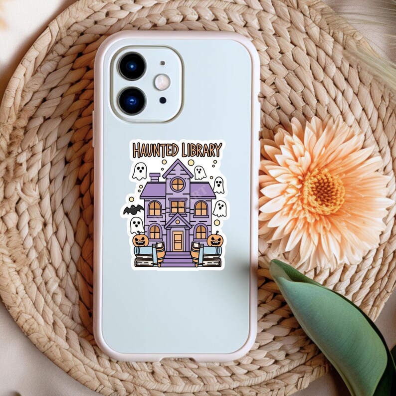 May include: A white phone case featuring a purple haunted library design. The design includes a spooky house with ghosts, bats, and pumpkins. The text "Haunted Library" is printed on the case.