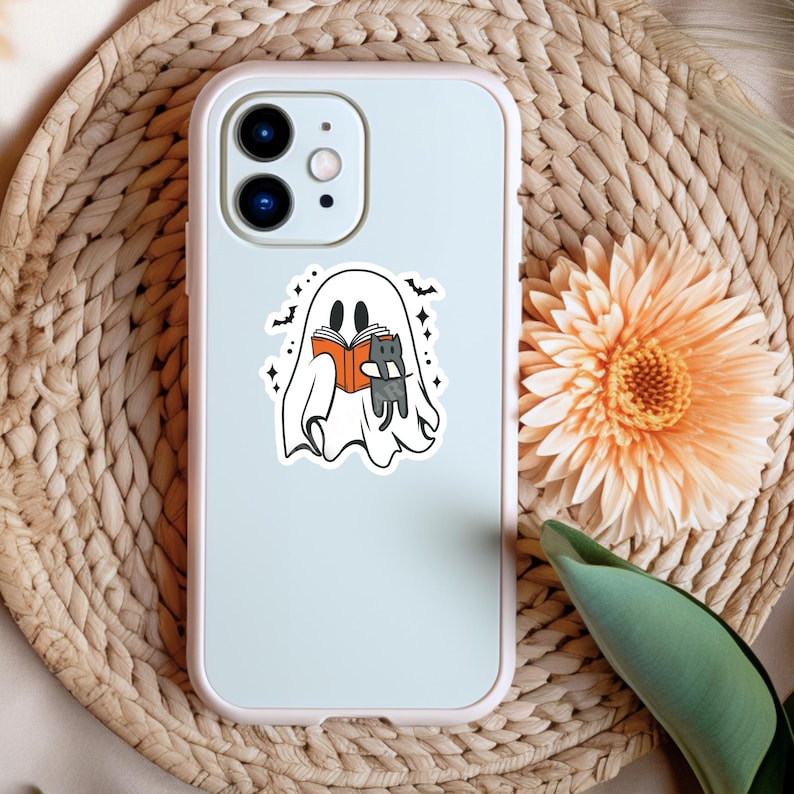 Peut inclure: Un fant&ocirc;me blanc tenant un livre et un chat noir dans ses bras. Le fant&ocirc;me est entour&eacute; d'&eacute;toiles et de chauves-souris. L'image est sur une coque de t&eacute;l&eacute;phone blanche.