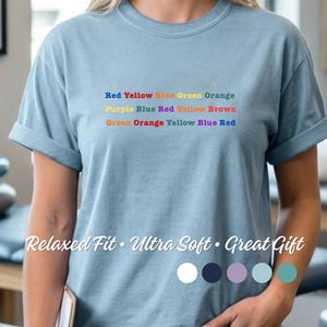 May include: A pale blue t-shirt with the words "Red Yellow Blue Green Orange", "Purple Blue Red Yellow Brown", and "Green Orange Yellow Blue Red" printed across the chest. The text "Relaxed Fit • Ultra Soft • Great Gift" is printed below the color names.
